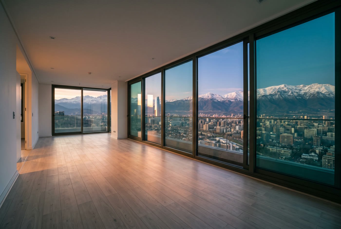 Living vacío de un departamento moderno en altura, con ventanal de piso a techo y vista a Santiago y la cordillera al atardecer.